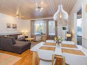 A modern living room with a sofa, dining table, and chairs, a ceiling fan, and a large window with curtains.
