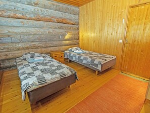 A log cabin room with two beds, a nightstand, and a wooden door.