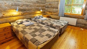 A log cabin bedroom with two beds, wooden floors, a window with a view, and a radiator.