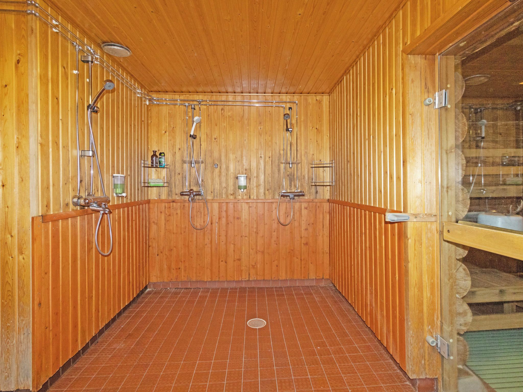Puinen sauna, jossa on useita suihkupäitä ja laatoitettu lattia.