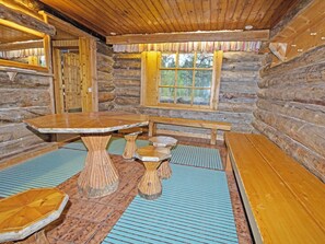 L’intérieur d’une cabane en rondins, avec une table en bois au centre, des bancs et une fenêtre.