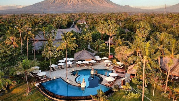 A resort with a large swimming pool, lounge areas, and thatched-roof huts, surrounded by palm trees and a mountain in the background. - Siddhartha Oceanfront Resort & Spa Bali (Kubu)