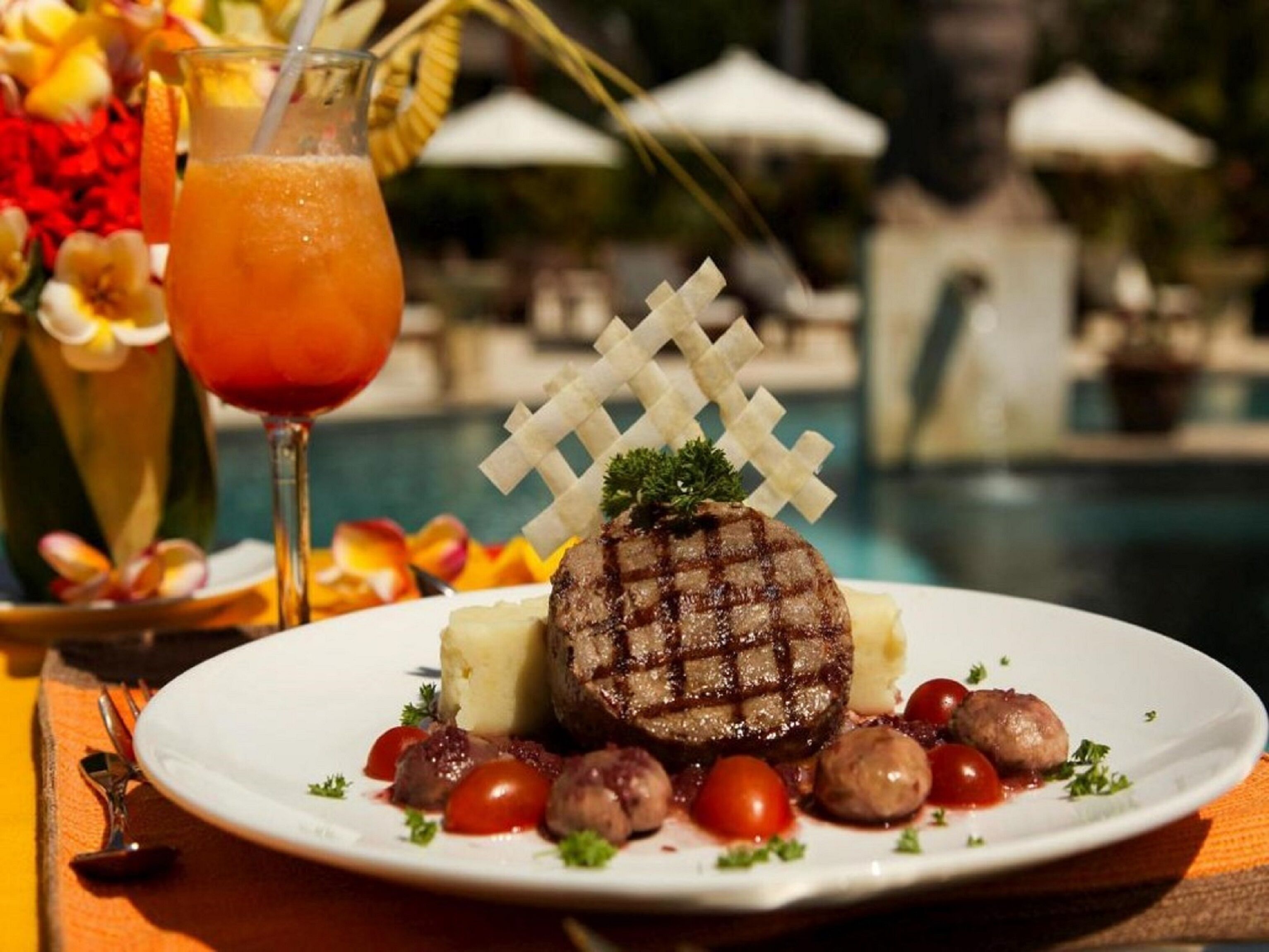 A plate of steak with a grilled pattern, served with potatoes, cherry tomatoes, and a side salad, accompanied by a glass of red drink.