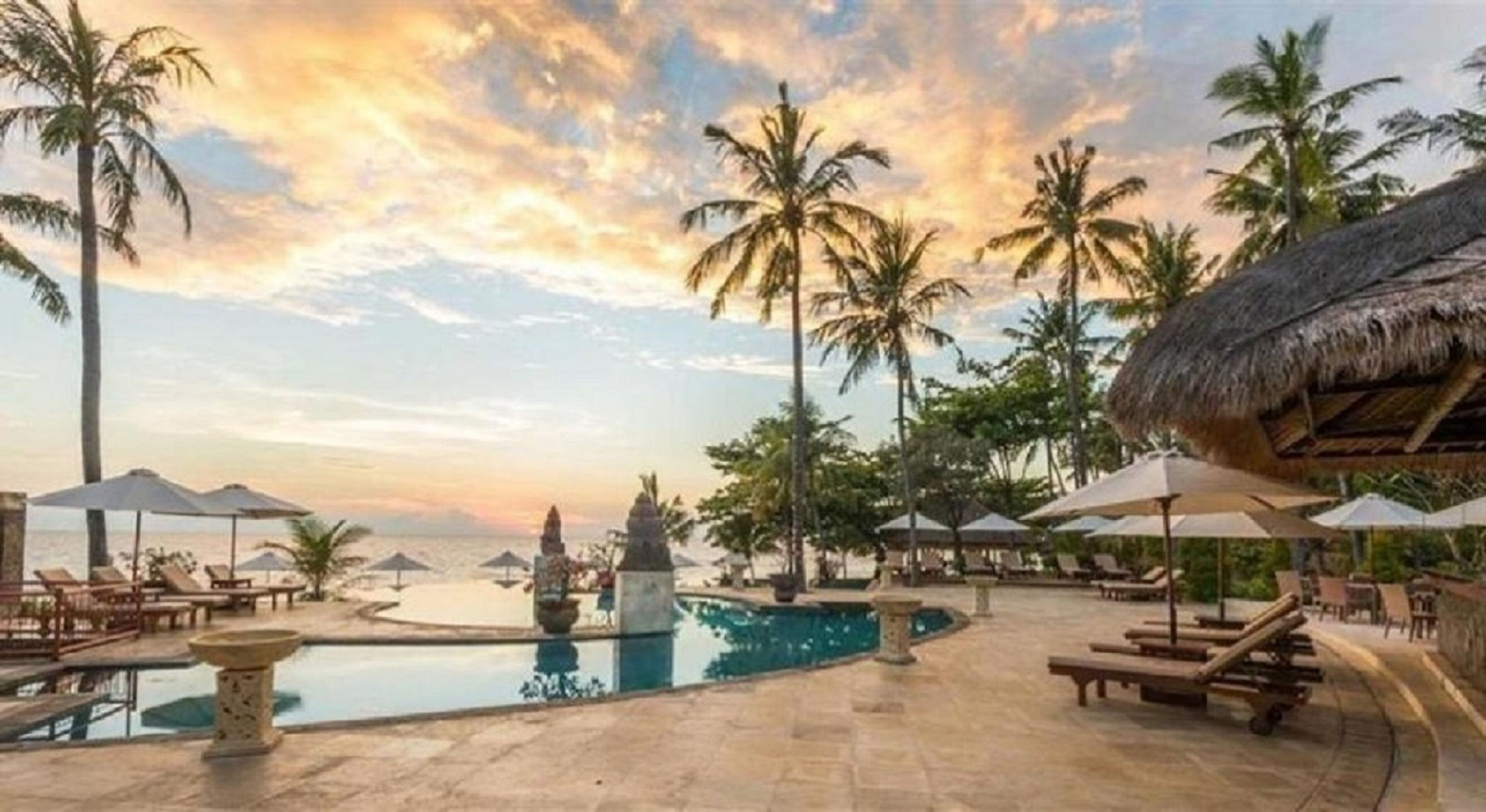 A resort pool area with lounge chairs, umbrellas, and palm trees.