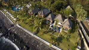 An aerial view of a resort with thatched-roof villas, a swimming pool, and palm trees. - Siddhartha Oceanfront Resort & Spa Bali (Kubu)