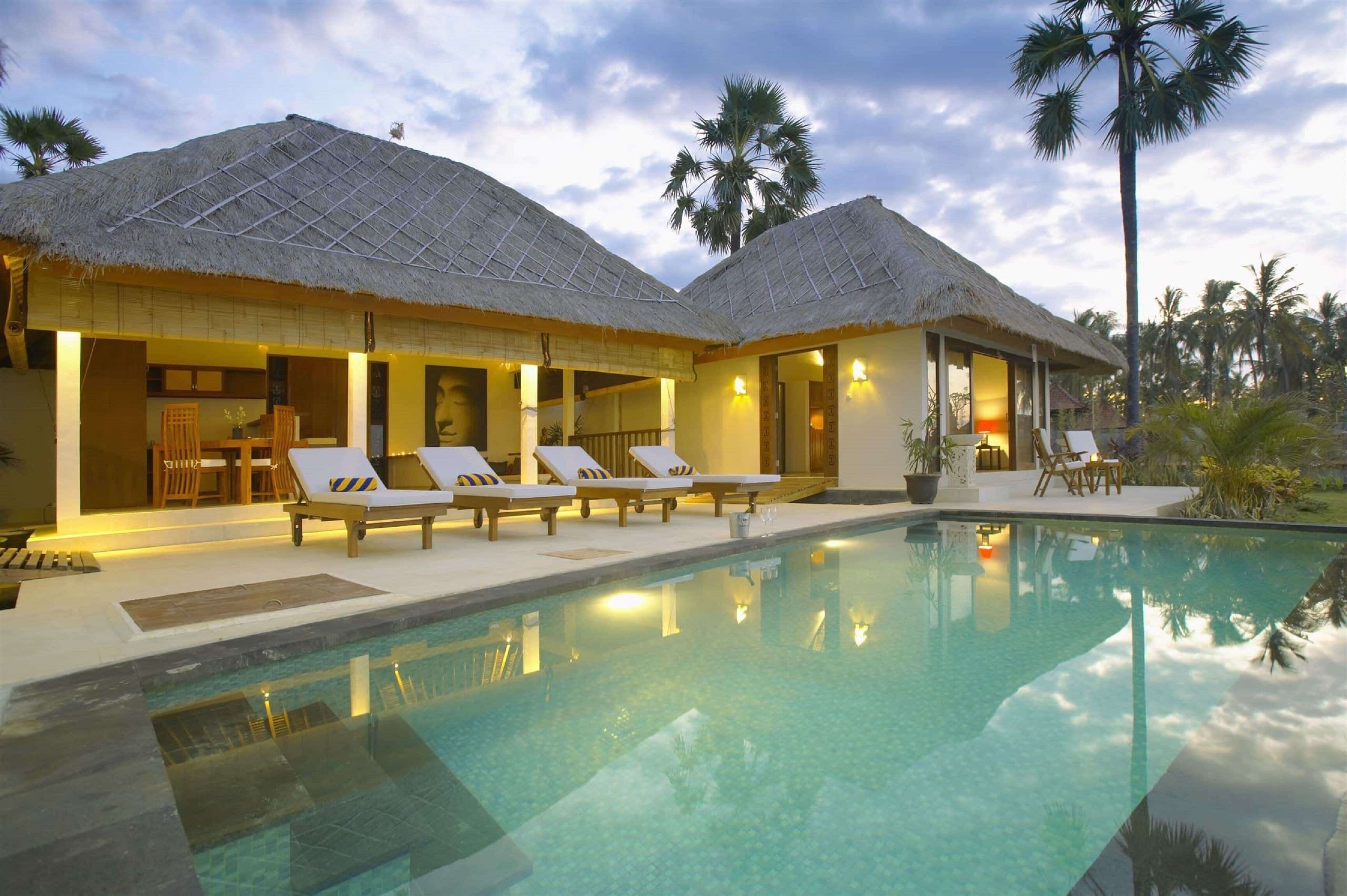 A resort with thatched-roof villas, a swimming pool, and palm trees.