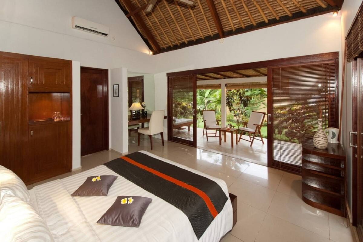 A hotel room with a bed, a desk, and a view of the garden.