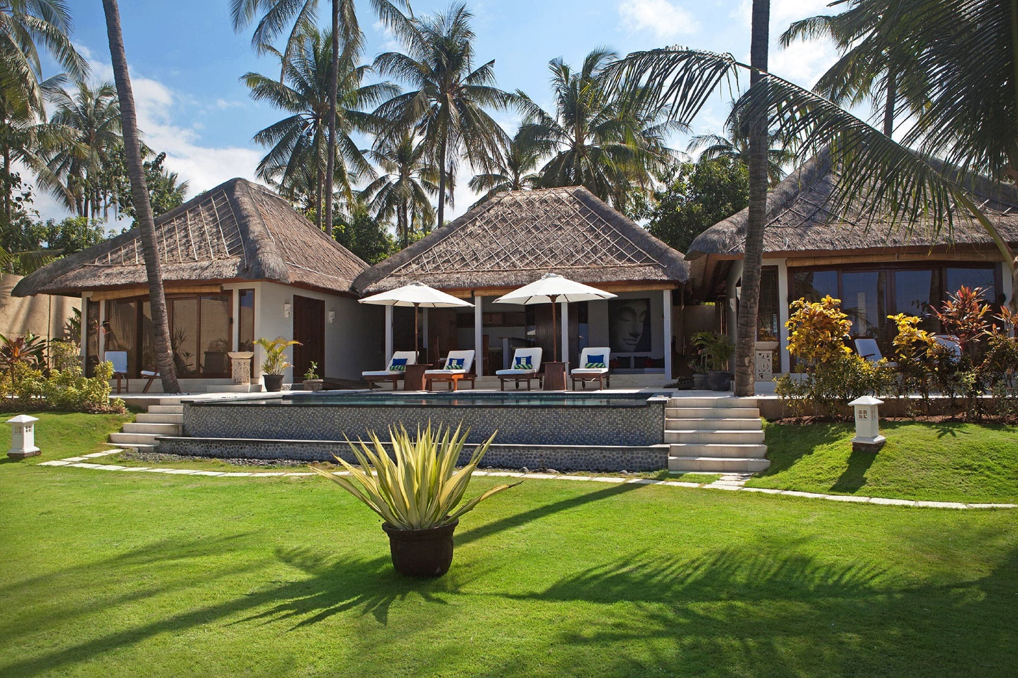A resort with thatched-roof bungalows, a swimming pool, and a well-maintained lawn.