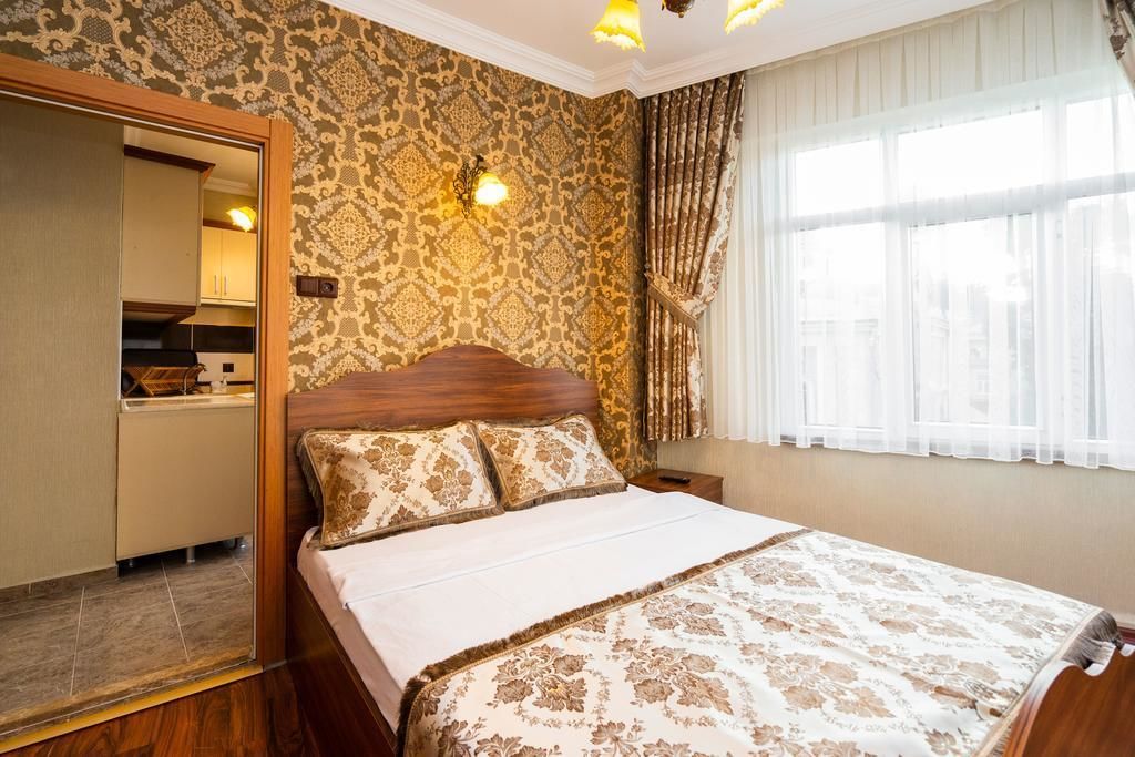 Ein Schlafzimmer mit einem großen Bett, einem Holz-Kopfteil, gemusterten Vorhängen und einem Fenster mit transparenten weißen Gardinen.