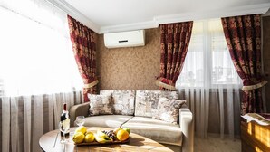 A modern living room with a beige sofa, a round wooden coffee table with fruits and a bottle, and red patterned curtains. - The First Ottoman Suites (Istanbul)
