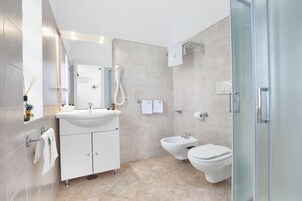 Un baño moderno con lavamanos, bidé, inodoro y cabina de ducha de cristal.