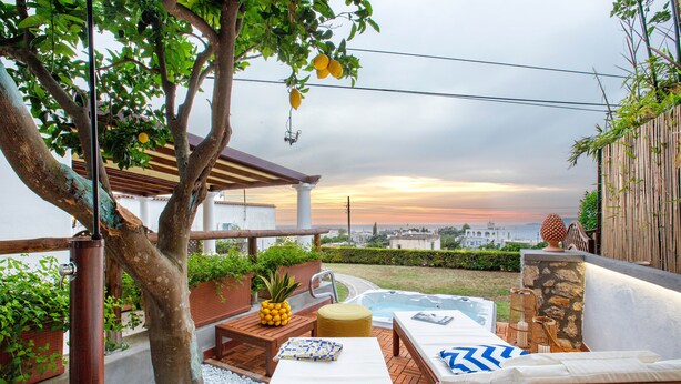 A patio with a pool, lounge chairs, a table with a pineapple, and a view of the sunset. - Relais Caposcuro (Anacapri)
