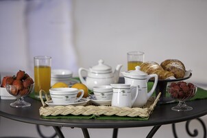 Ein Frühstücksaufstellling mit weißen Keramikgeschirr, einer Karaffe, Gläsern und Gebäck auf einem runden Tisch.