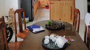 A modern kitchen with wooden cabinets, a refrigerator, and a dining area with a table set for tea.