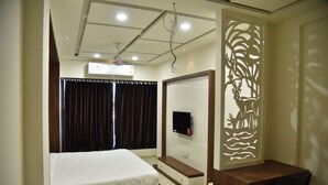 Un dormitorio con cama, escritorio, silla, televisor y un panel decorativo en la pared.