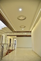 Um corredor espaçoso e bem iluminado, com design moderno no teto, escada com guarda-corpos de metal e piso ladrilhado.