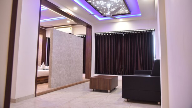 Una sala de estar moderna con ventilador de techo, un sofá negro, una mesa de centro de madera y un ventanal con cortinas oscuras.