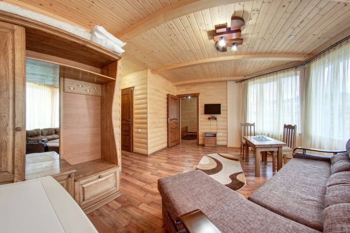 A log cabin interior with a wooden floor, a sofa, a dining table, and a TV mounted on the wall.