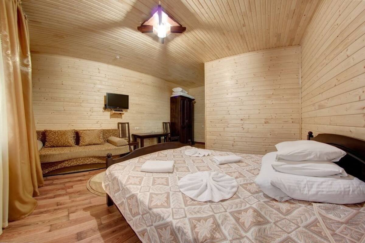 A wooden cabin room with a bed, a sofa, a television, and a wooden ceiling.