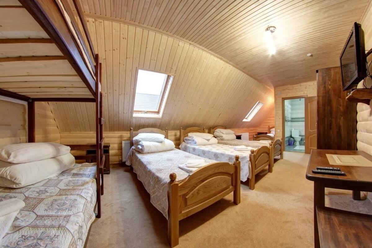 A cozy attic bedroom with three wooden beds, a TV, and a small table.