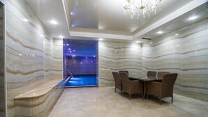 Uma área de spa com parede de mármore, piscina e zona de refeições com mobiliário de vime.