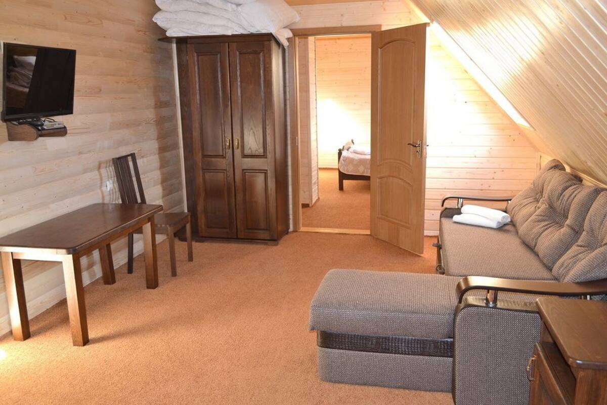 A cozy room with a wooden floor, a bed with a gray blanket, a small table, a TV, and a wardrobe.