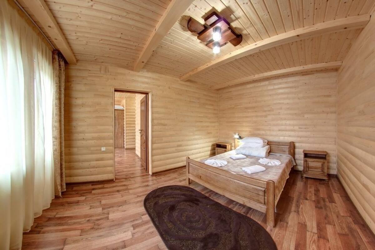 A wooden-paneled room with a bed, a nightstand, and a door leading to another room.