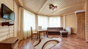 Interior de uma cabana de tronco com teto de madeira, televisão na parede, um sofá, uma mesinha e um frigorífico.