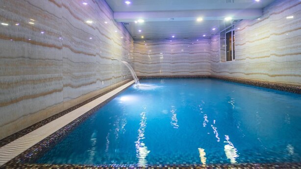 Piscina interna com design de parede em mármore, superfície de água cristalina e uma pequena janela lateral.