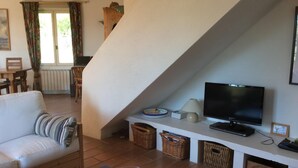 Un soggiorno con un divano bianco, una TV a schermo piatto, cesti di vimini e una scala.