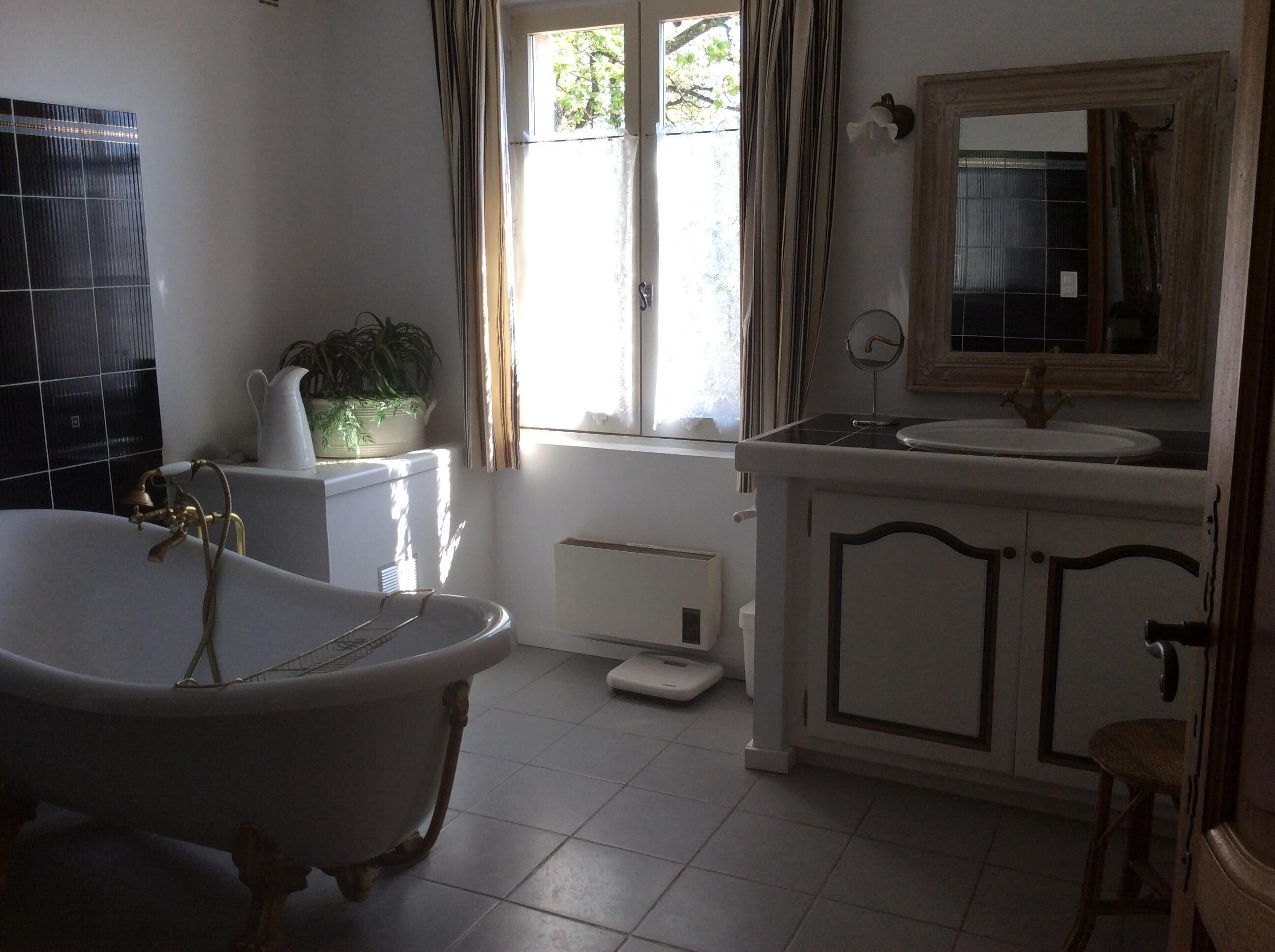 A bathroom with a freestanding bathtub, a white sink with a mirror above it, and a window with curtains.