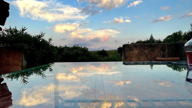 Cielo sereno con nuvole, piscina con bordo piastrellato e muro in pietra sullo sfondo.