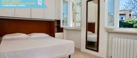 A bedroom with a bed, a large window, a mirror, and a view of the outside.