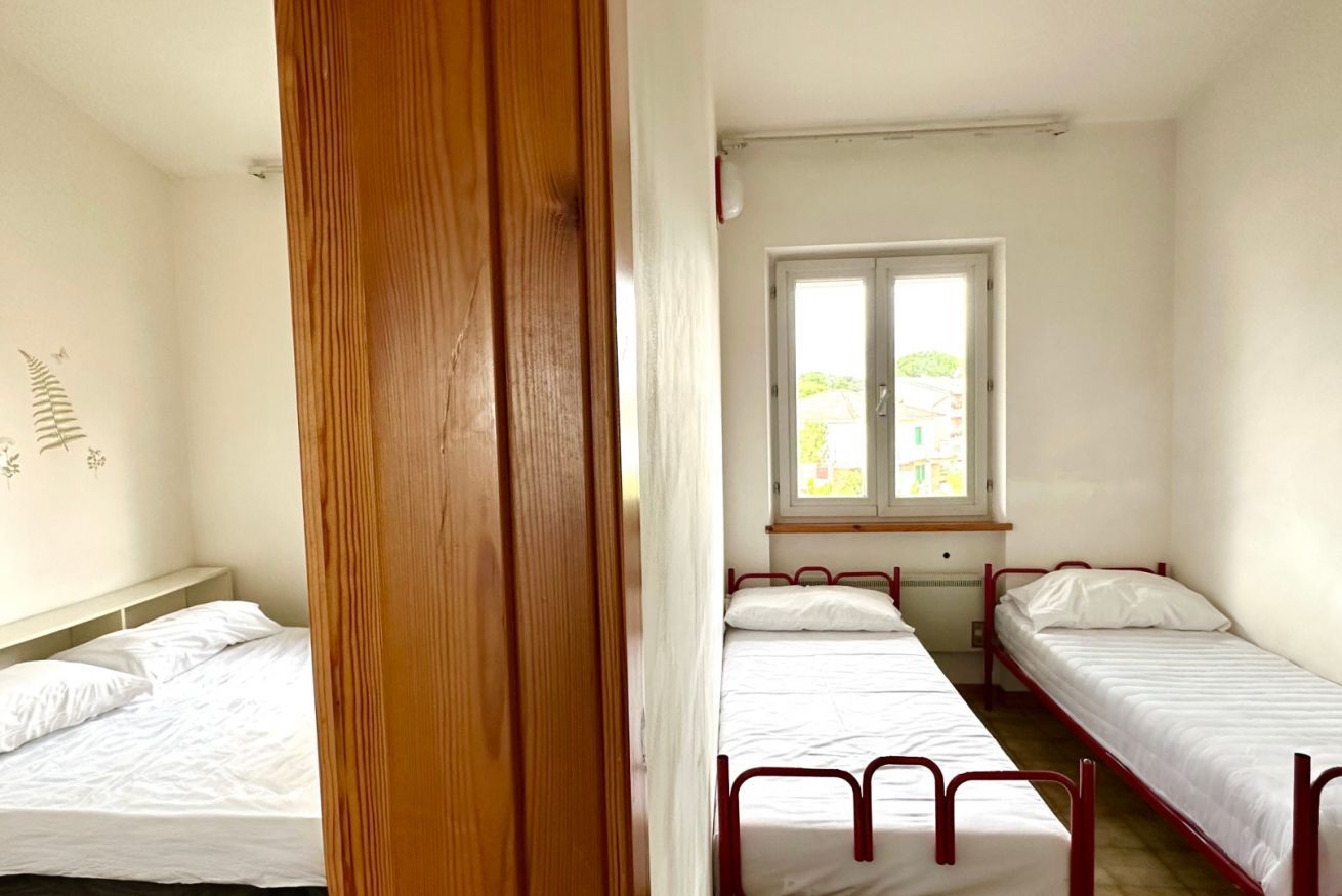 Une chambre avec deux lits simples, une porte en bois et une fenêtre donnant sur un paysage verdoyant.