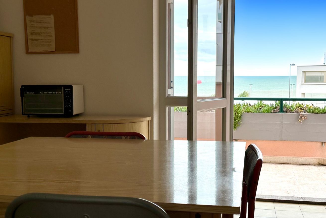 Une chambre avec une table en bois, un four à micro-ondes et une vue sur l’océan par une porte vitrée.