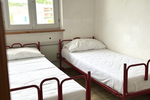 A small, clean room with two single beds, a window, and a radiator.