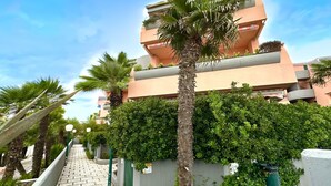 Un edificio de varios pisos con balcones, un paseo empedrado y palmeras.