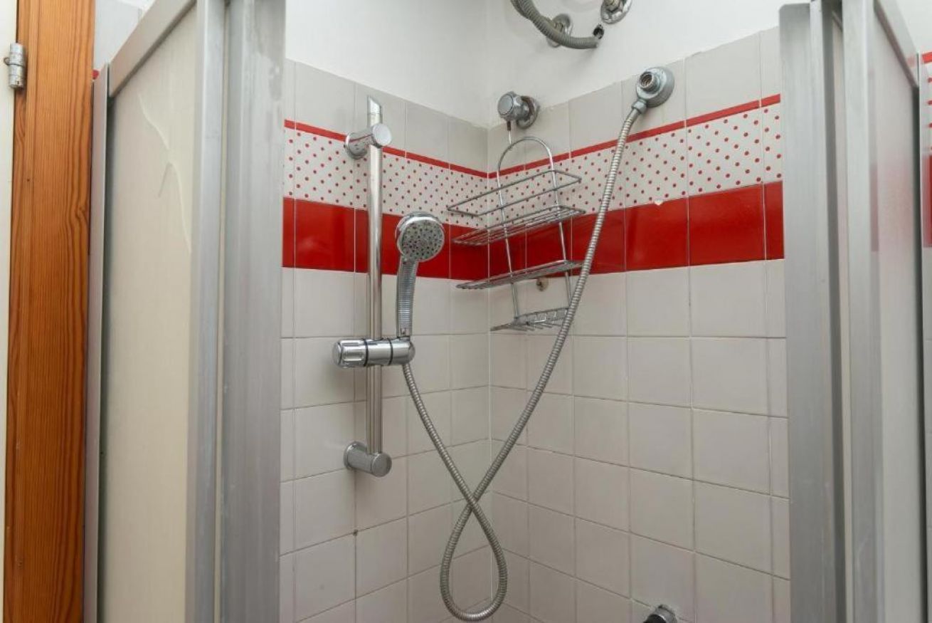 Une douche équipée d’un pommeau de douche chromé, d’un pommeau de douche à main et d’une étagère fixée au mur.