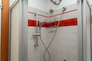 Doccia con soffione cromato, doccetta a mano e ripiano a parete.