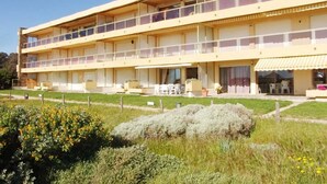 Un hotel de dos pisos con techo plano, varios balcones y una zona de estar al aire libre cubierta.