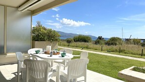 Un patio con una mesa y sillas, una planta en maceta y vistas al mar y a las colinas.