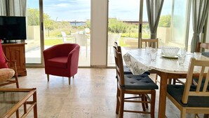 Una habitación con una mesa de comedor, sillas, un televisor y vistas a un jardín a través de amplios ventanales correderas.