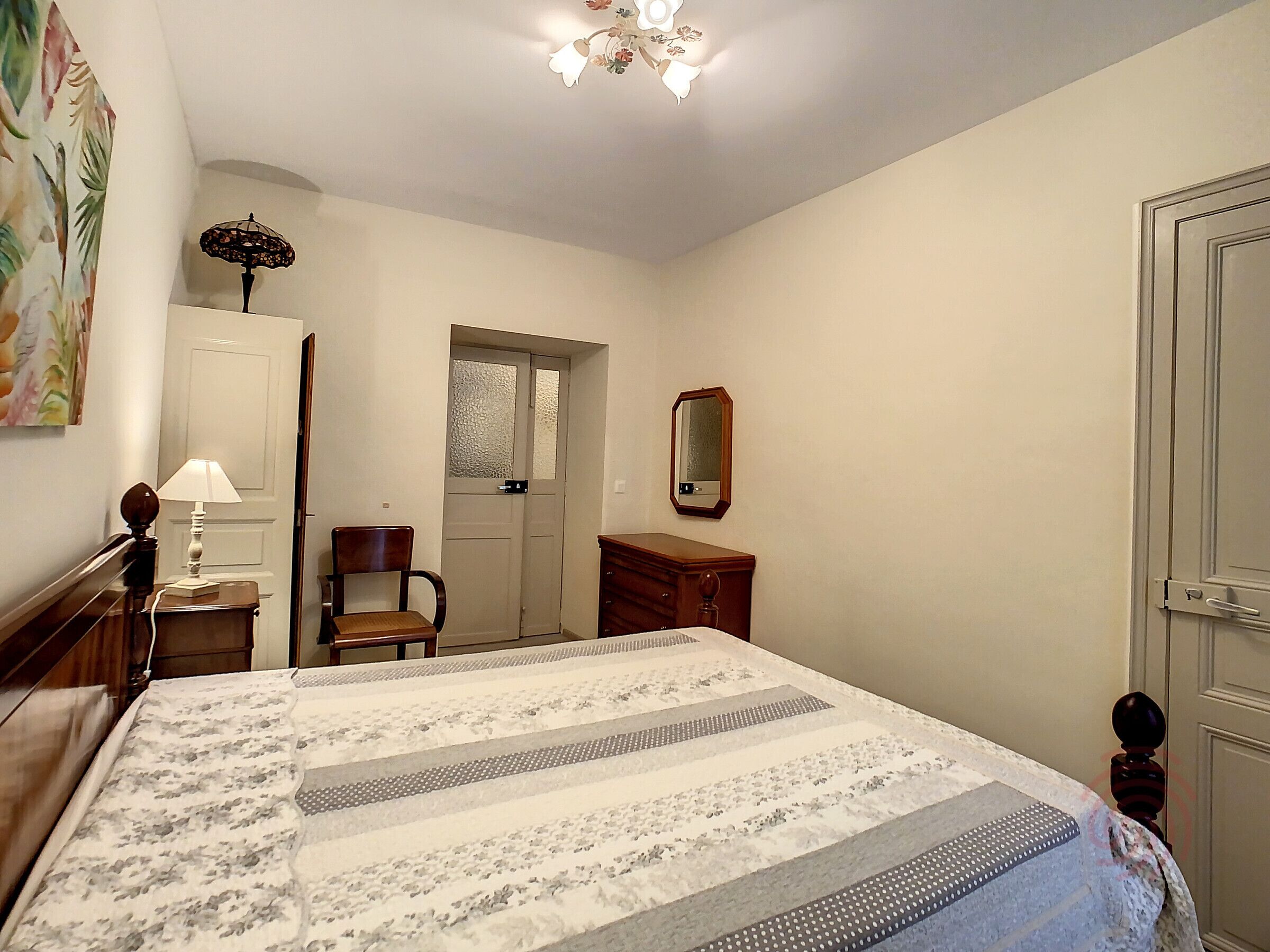 A bedroom with a bed, a chair, a dresser, a mirror, and a door.