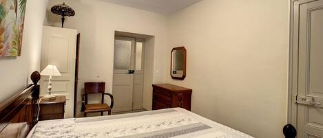 A bedroom with a bed, a chair, a dresser, a mirror, and a door.