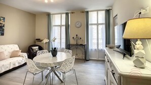 Ein Wohnzimmer mit einer Couch, einem Esstisch, Stühlen, einem Fernseher und einer Lampe.