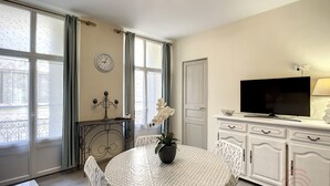 Ein gut beleuchteter Raum mit rundem Tisch, Stühlen, einem Fernseher und einer Uhr an der Wand.