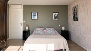 Een slaapkamer met een bed, twee nachtkastjes, een kledingkast en twee ingelijste foto’s aan de muur.
