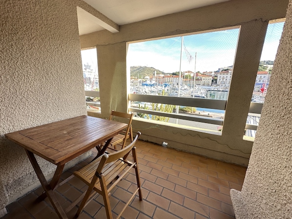 A balcony with a wooden table and chairs, a view of a marina with boats, and a cityscape in the background.