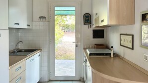 Una cucina con mobili bianchi, un lavello e una porta che dà su uno spazio esterno.