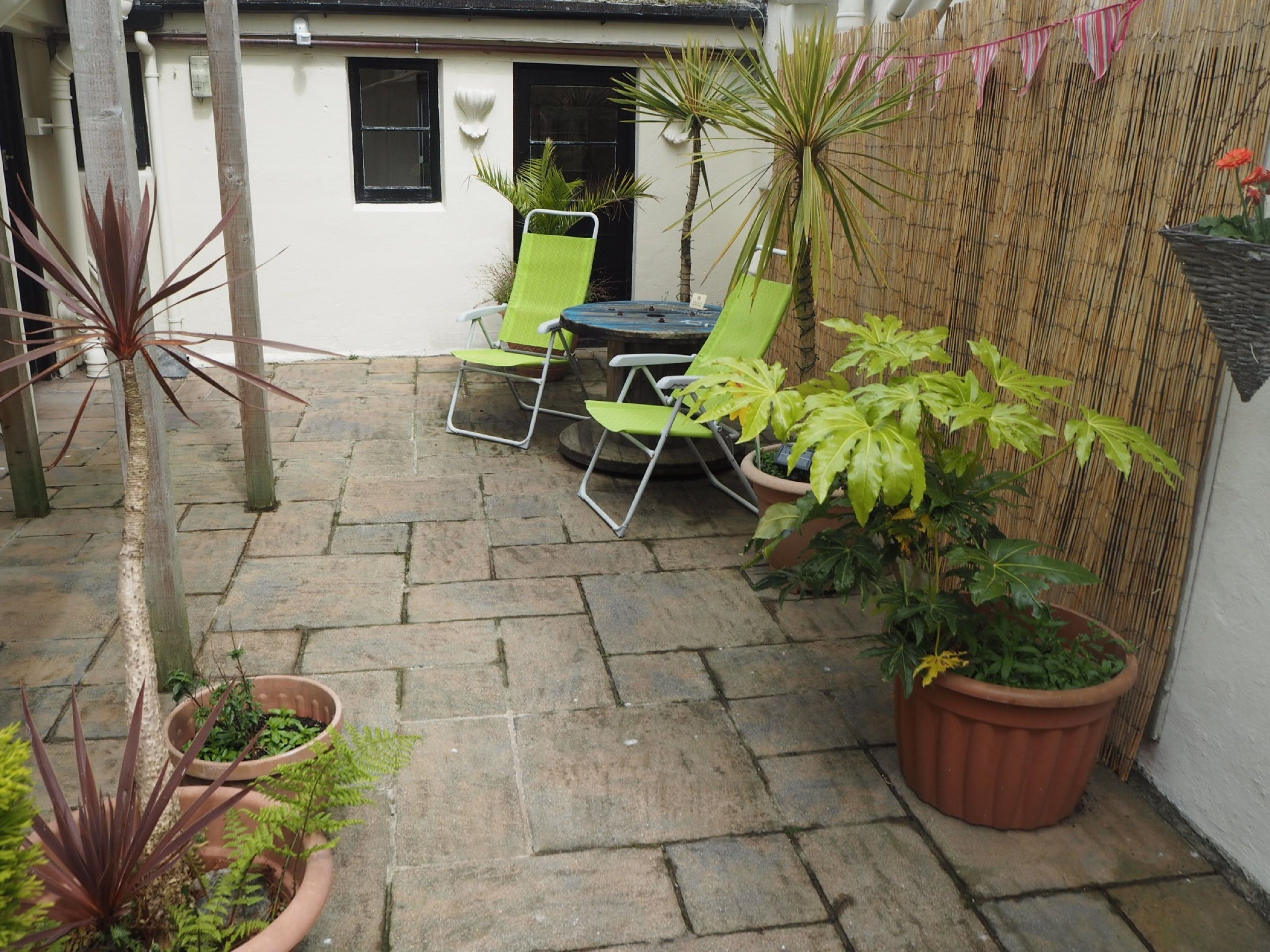 Un espace patio avec un sol en pierre, des chaises vertes, une table et des plantes en pot.